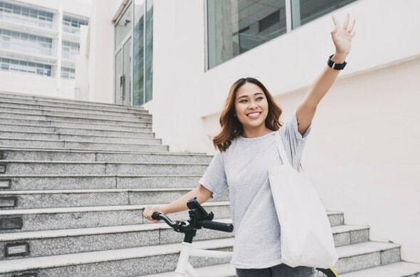 Menina dando tchau para alguém enquanto vai embora em uma bicicleta